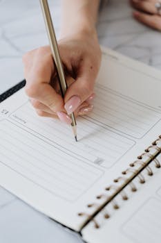 A close-up of a hand writing in a planner with a pencil. Ideal for organization themes.