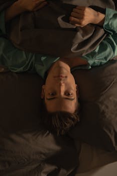 A young man lies awake in bed, struggling with insomnia under dim lighting.