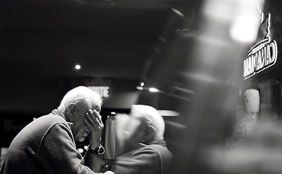 Black and white image of an elderly man reflecting in a café setting.