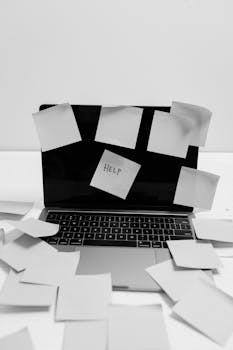 Black and white photo of a laptop covered with sticky notes, one labeled 'HELP'.