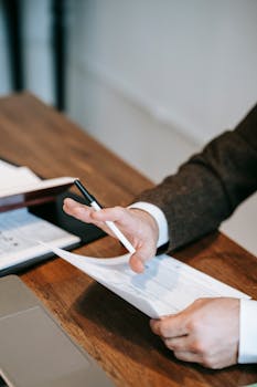 Close-up of a businessman in a suit analyzing papers on a wooden desk.