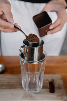 Close-up of coffee preparation using metal filter and glass cup.