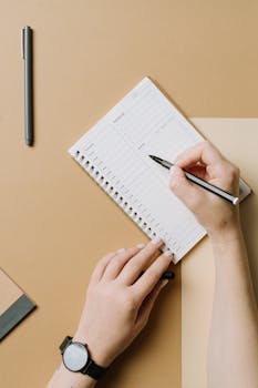 Close-up of hands writing in a planner on a brown desk, perfect for organizing and planning concepts.