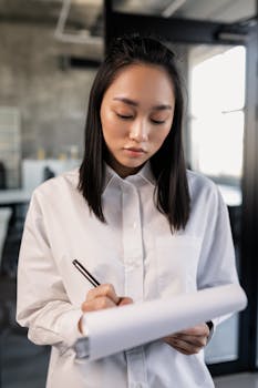 Focused young woman writing on a notepad in a modern workspace.