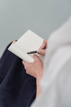 Person holding a notebook and pen, focused on writing or drawing.