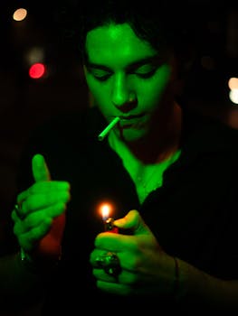 Man lighting a cigarette under green light in an urban night scene, creating a moody atmosphere.
